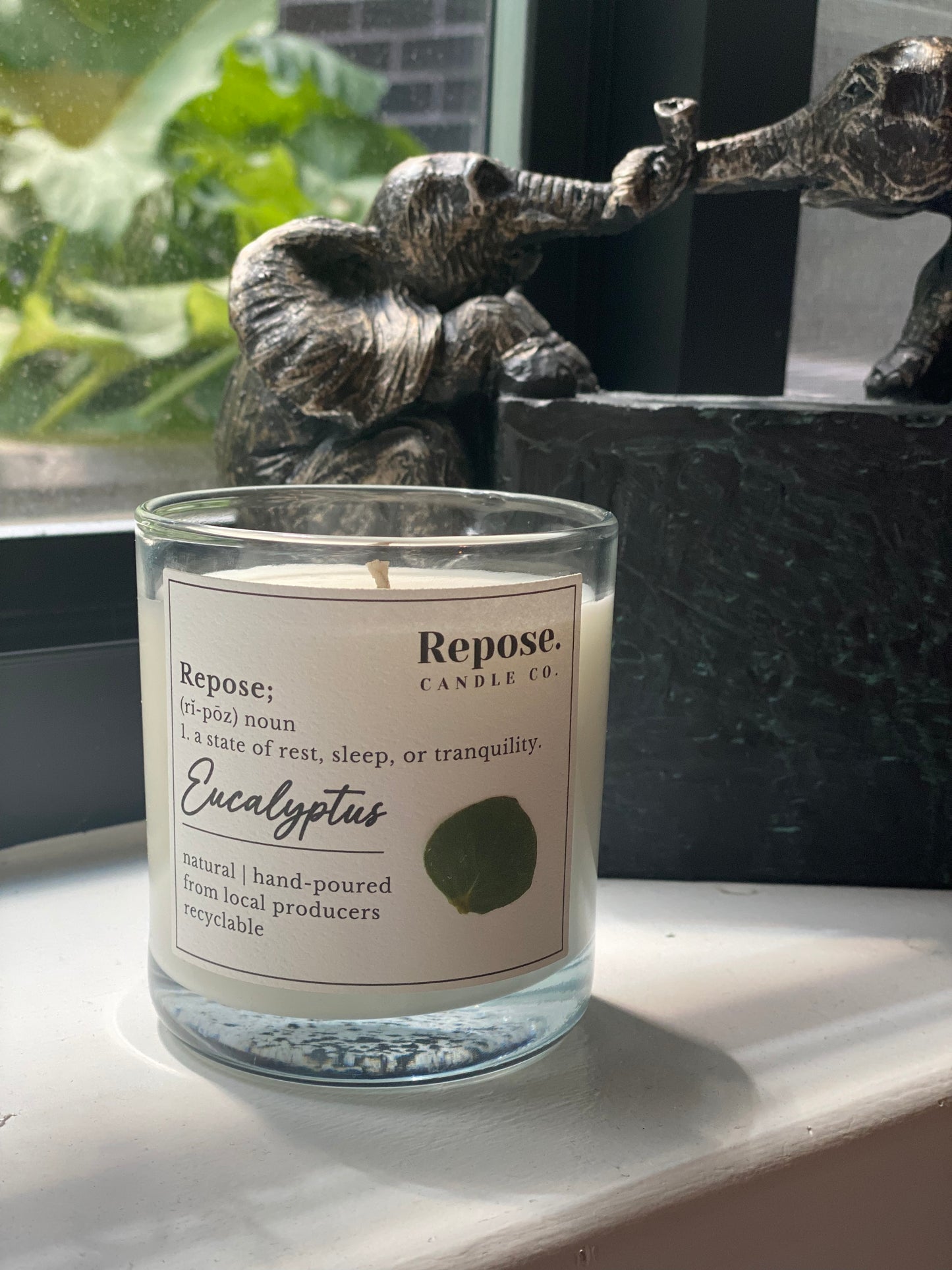 A Eucalyptus Candle next to a window in front of an elephant figurine.