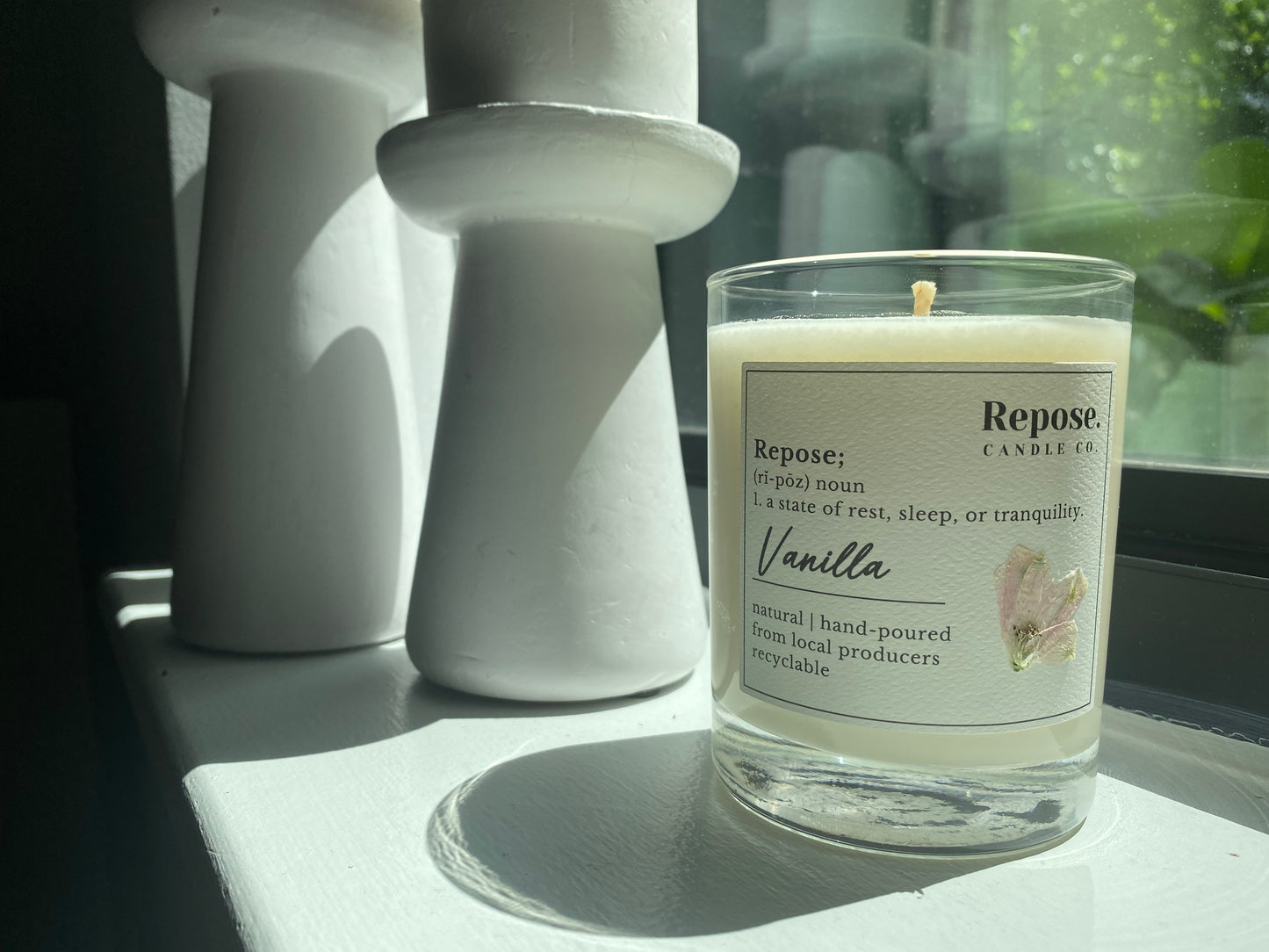A vanilla candle next to a window in front of two pillar candles.
