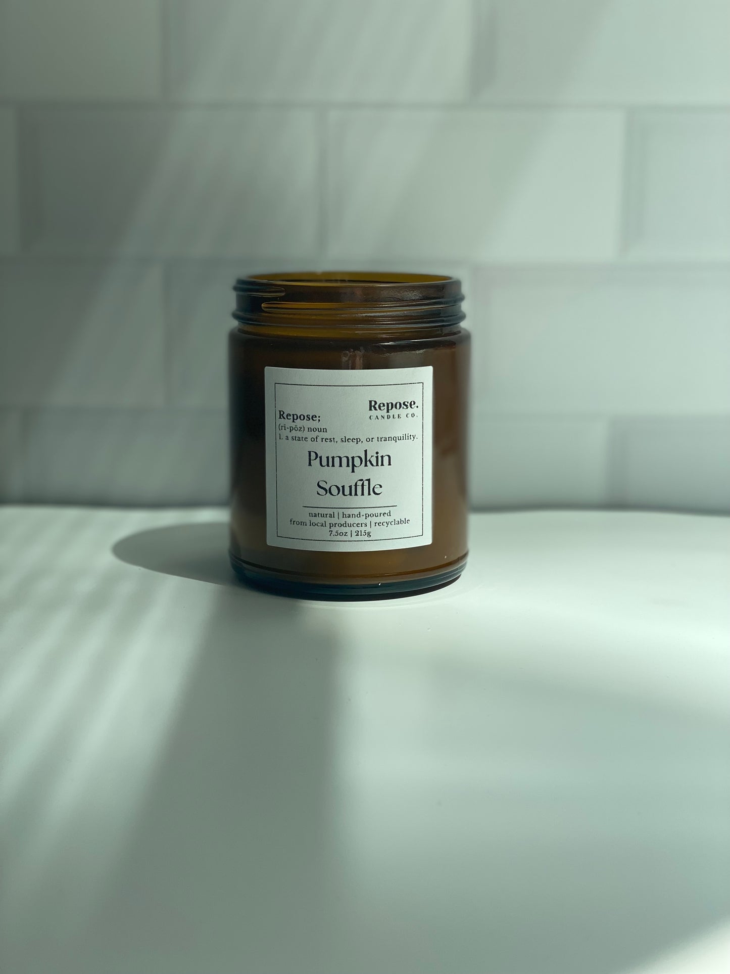 Pumpkin souffle candle in front of white subway tile background.