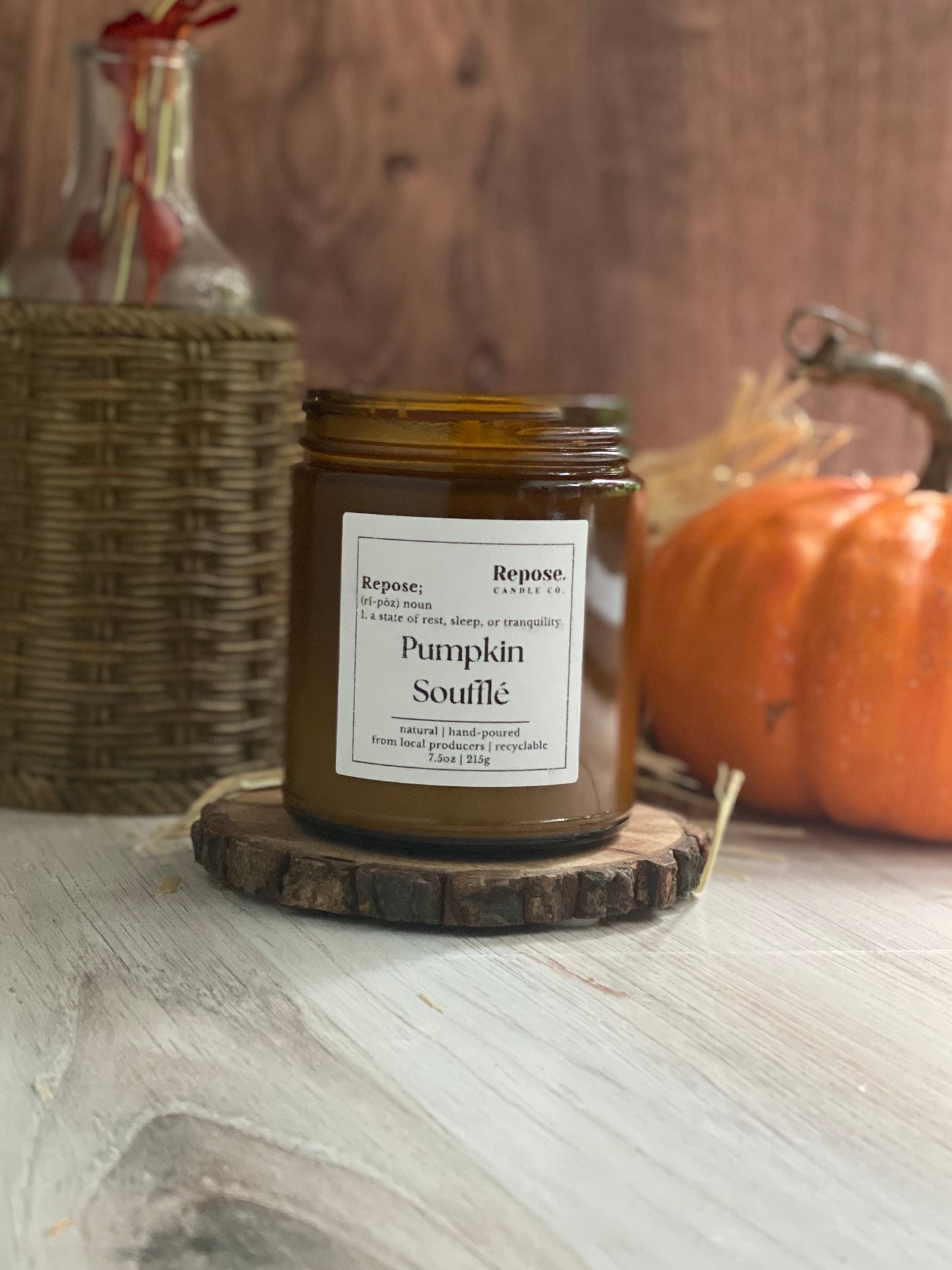 Pumpkin souffle candle in front of a pumkin and a vase.