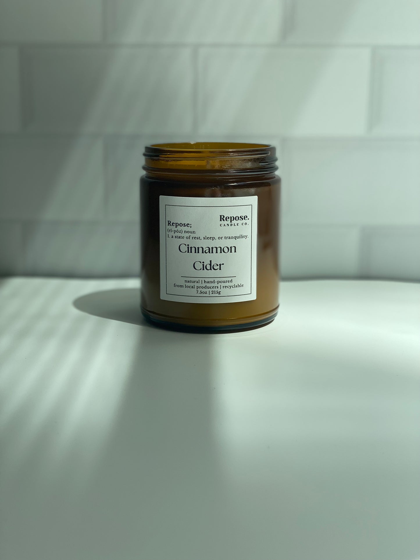 A cinnamon cider candle in front of a subway white tile background.